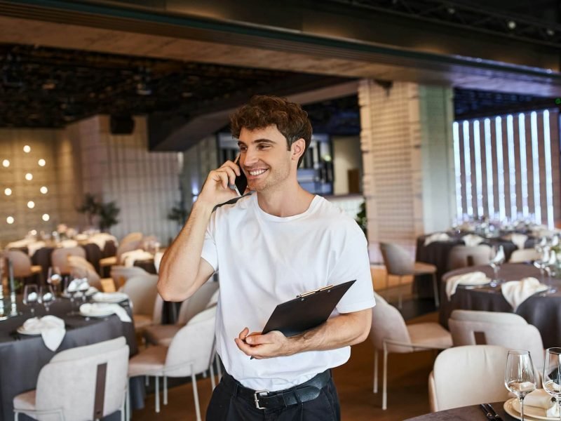 smiling-event-organizer-with-clipboard-talking-on-smartphone-near-festive-tables-in-banquet-hall.jpg